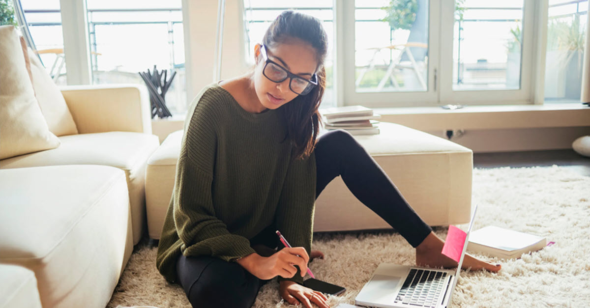 College aged woman studying on floor with computer.