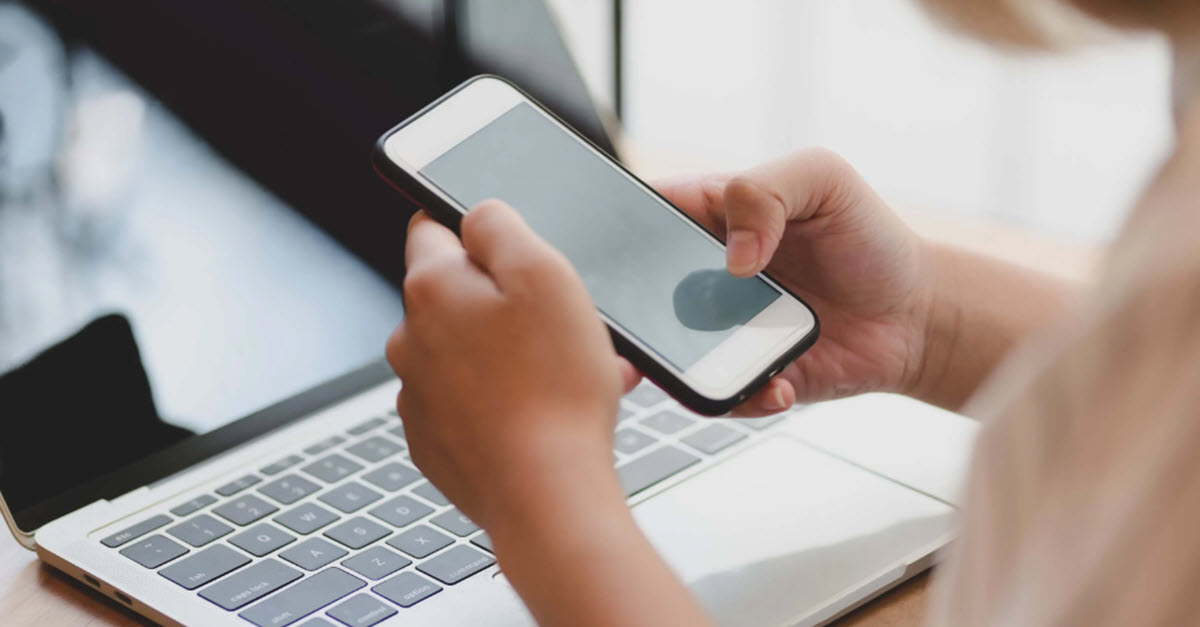 Woman browsing on her phone by her computer